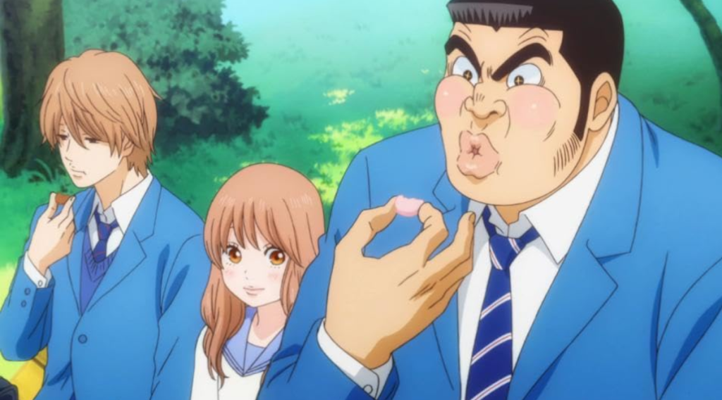 Three high school anime characters, the boys in blue uniforms and the girl wearing a white and light blue sailor suit (Anime: My Love Story). sitting on a park bench eating sweets. On the left is Makoto Sunakawa with light brown hair. In the center is Rinko Yamato with rosy light brown hair. On the left is Takeo Goda with jet black buzz cut style hair. 